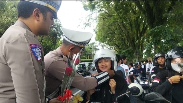 Caption: Satlantas Polres Jembrana bersama komunitas otomotif , ojol dan pelajar bagikan bunga dan gantungan kunci salam kampanye keselamatan berkendara di jalan Sudirman Jembrana, Sabtu (25/10/25). (wacanabali/Dika)